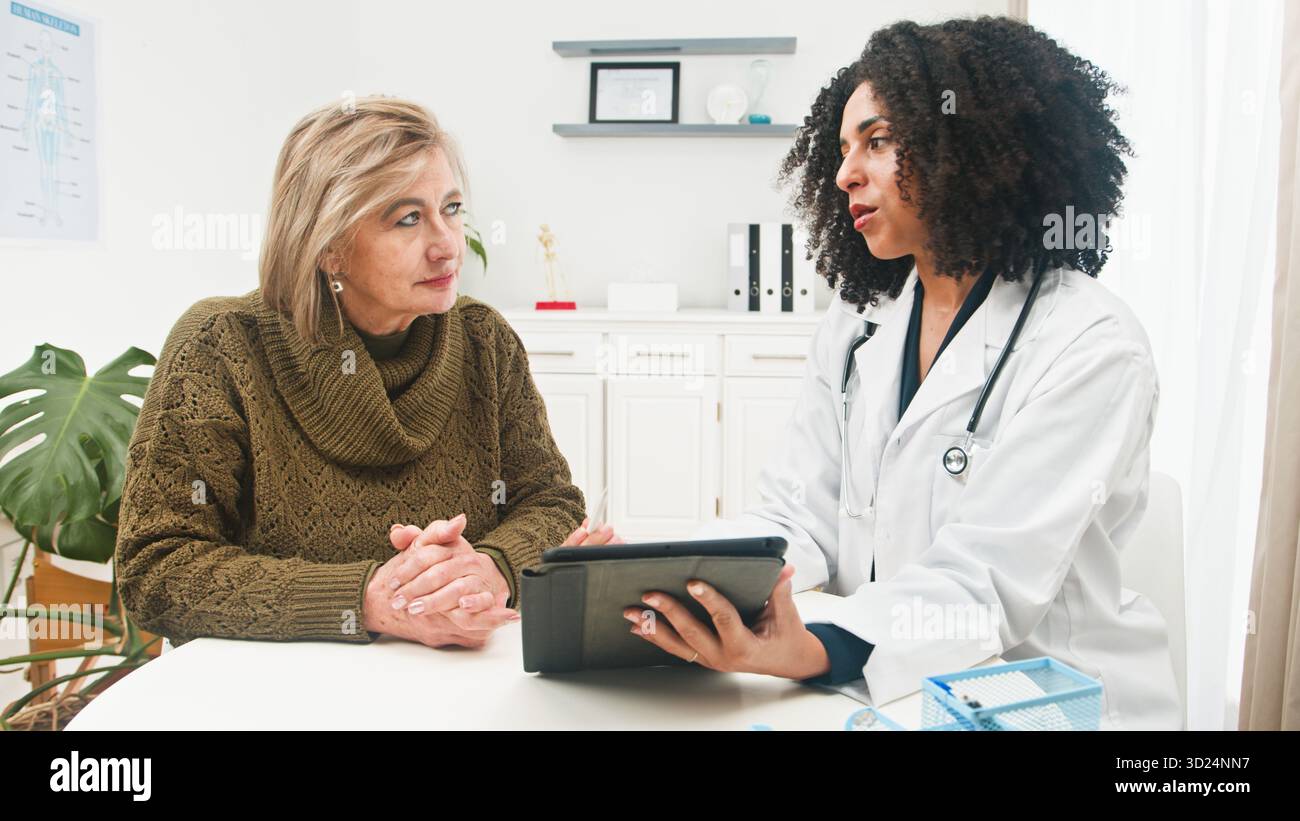 Il medico consulta il paziente in clinica con la compressa, fornendo consigli medici compassionevoli durante la sessione di Checkup Foto Stock