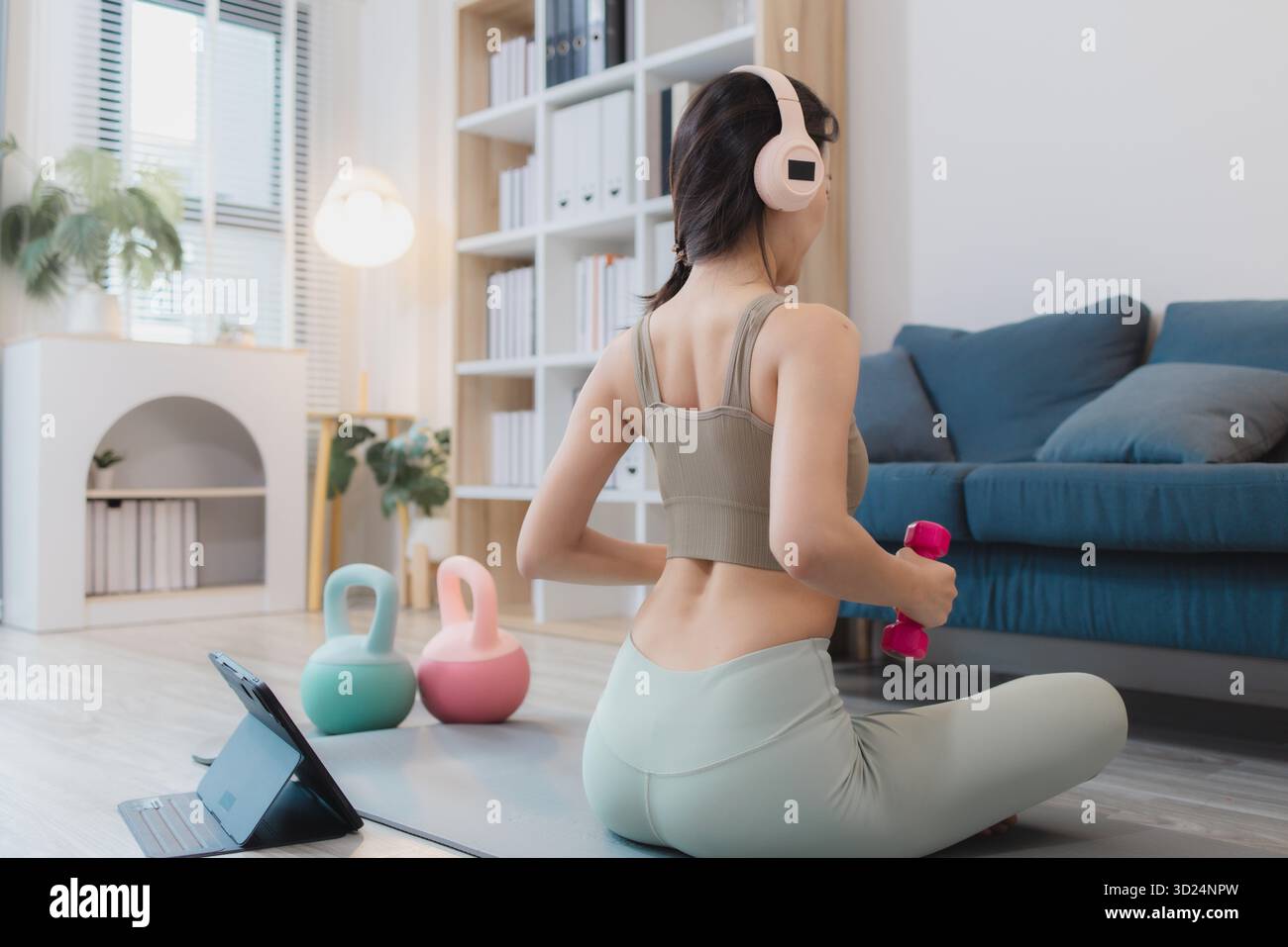 Una giovane donna si sta esercitando a casa, praticando yoga e allenamento di forza con manubri e kettlebell su un tappetino. Segue la sua routine di allenamento wi Foto Stock