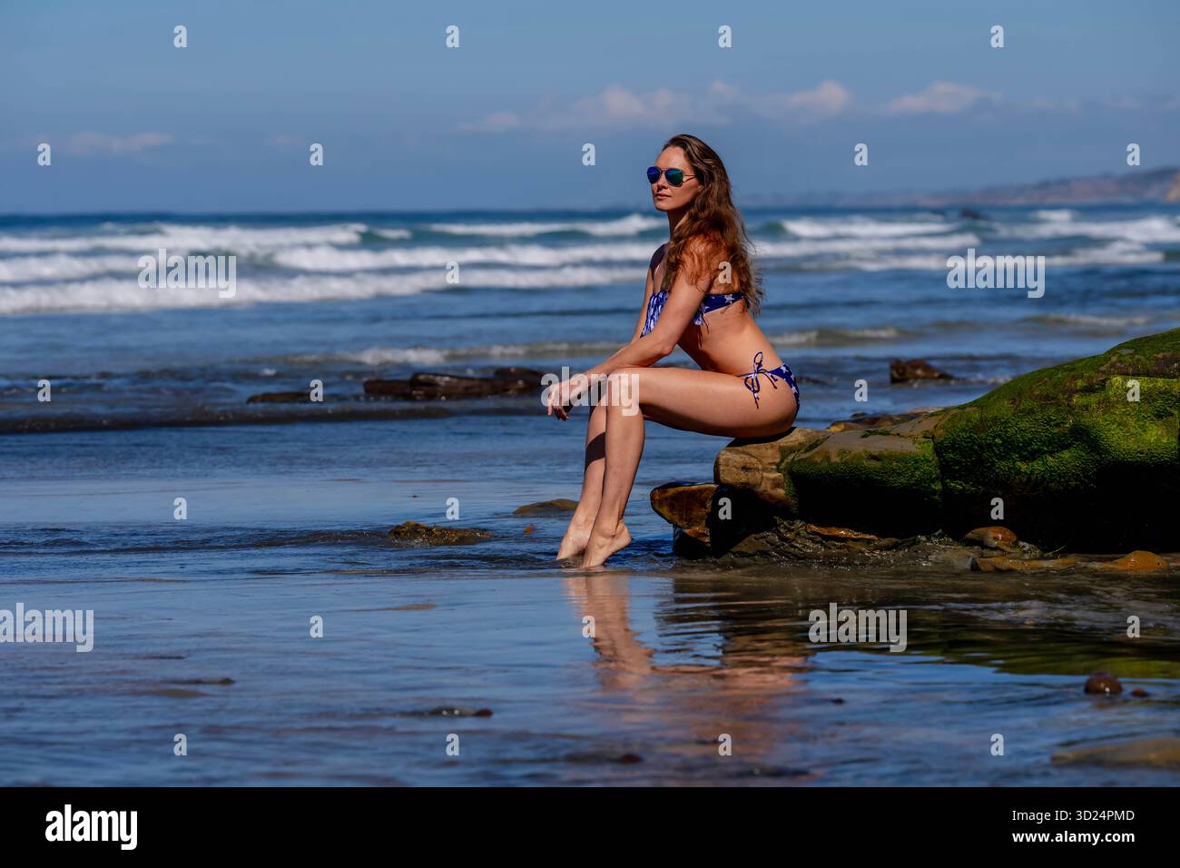 Una donna mozzafiato si crogiola nella beatitudine della spiaggia, vicino a un molo, sotto cieli azzurri, abbracciando la serenità di una giornata perfetta in riva al mare Foto Stock