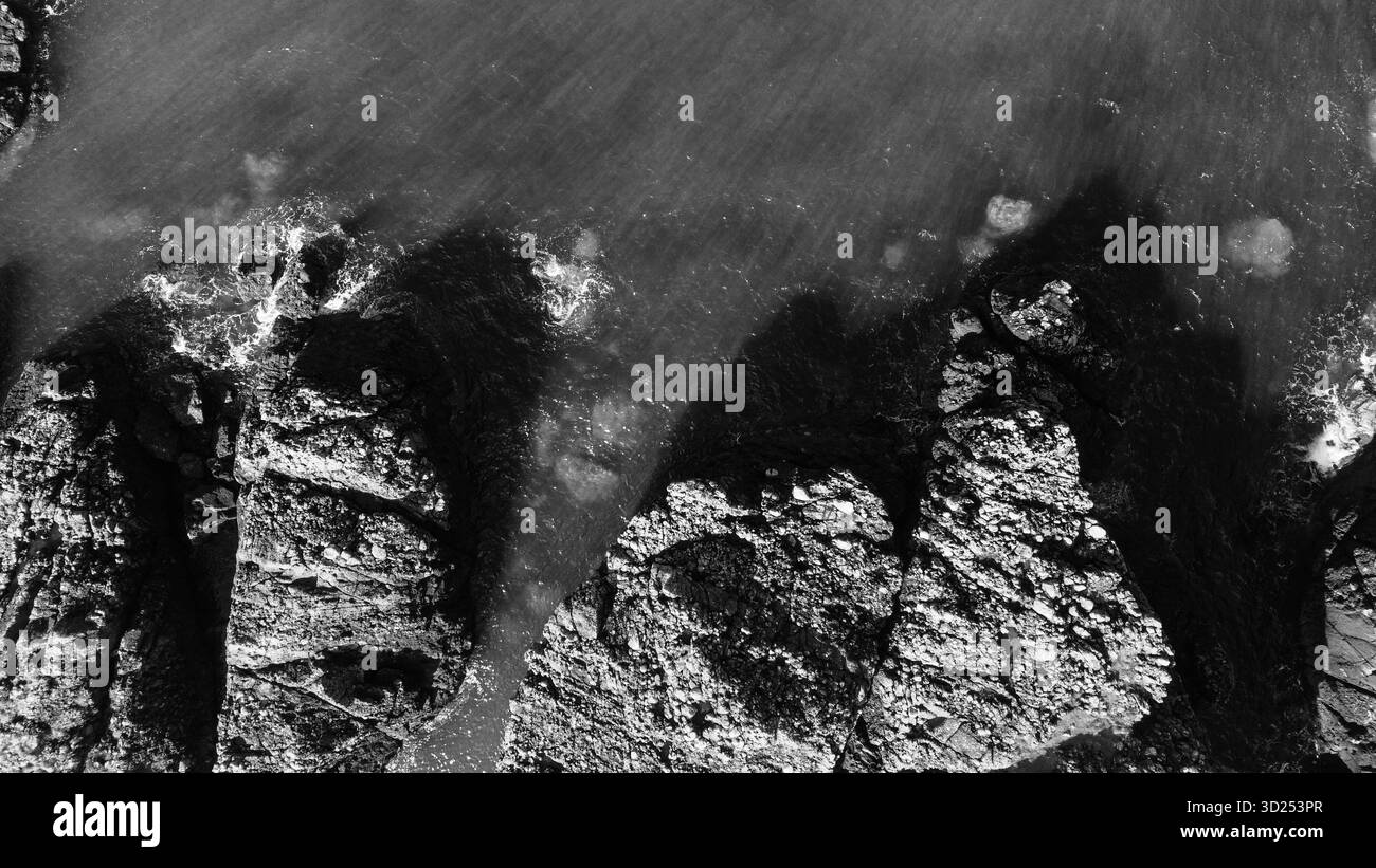 Vista aerea in bianco e nero delle onde del mare che si infrangono contro le rocce costiere Foto Stock