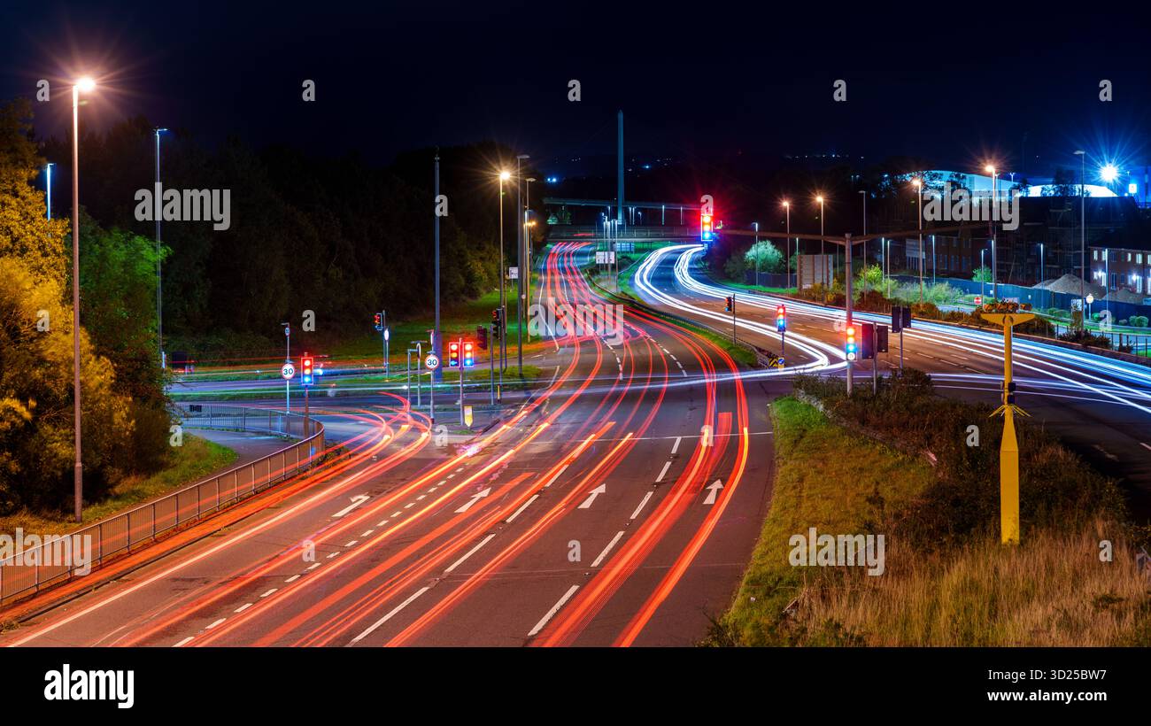 Il traffico si muove rapidamente su una strada trafficata a un incrocio, formando piste luminose dinamiche e riflessi luminosi Foto Stock