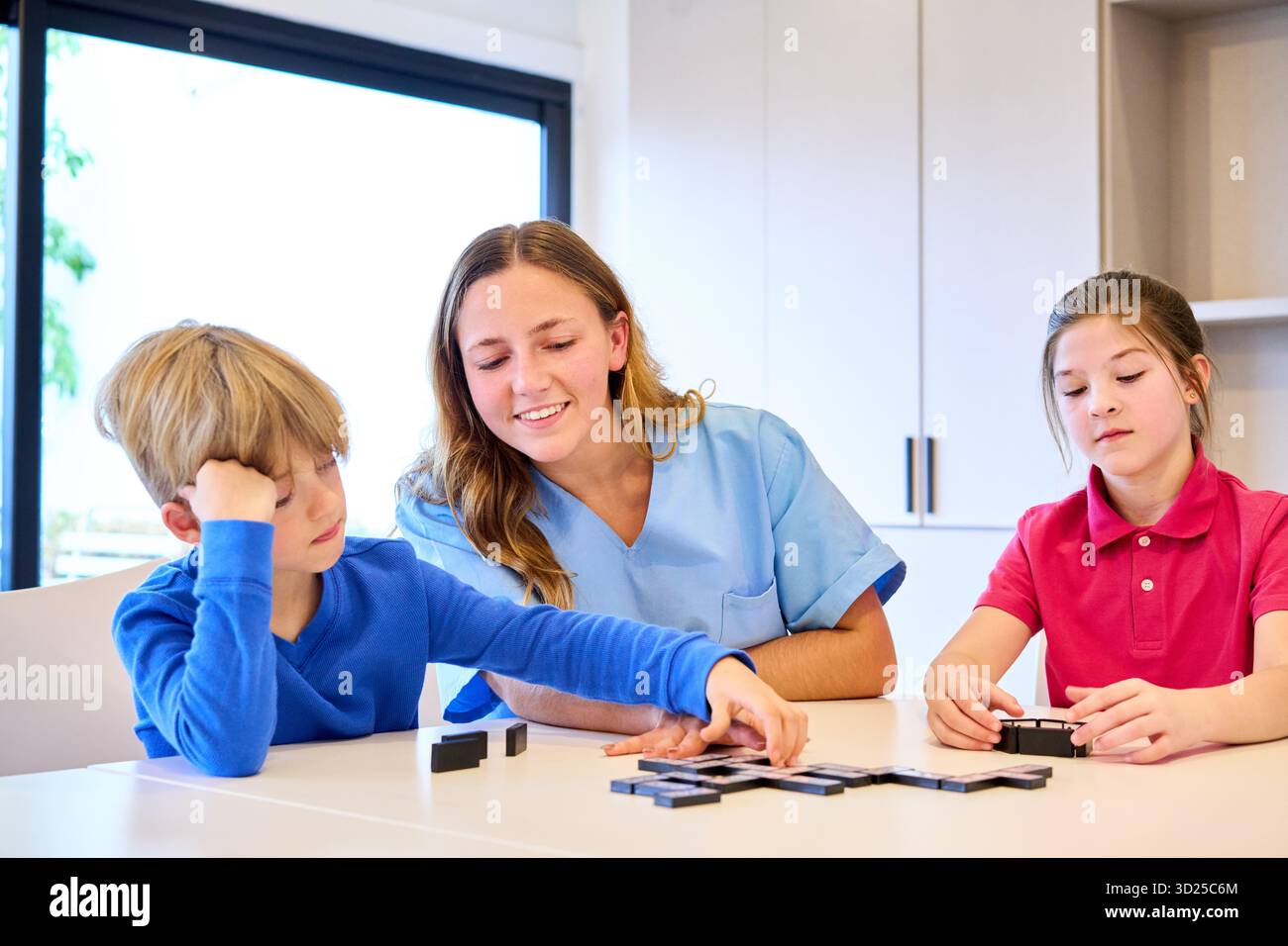 Un terapeuta assistenziale guida due bambini attraverso un'attività di riabilitazione pediatrica in una clinica luminosa. Lavorano sulle capacità motorie e sull'equilibrio con simp Foto Stock