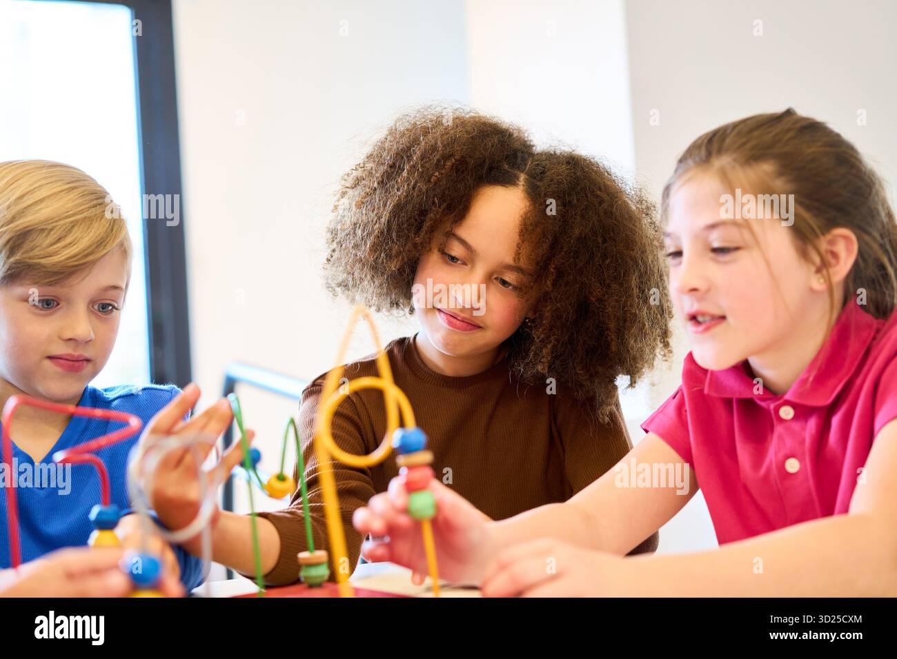 Tre bambini collaborano a un labirinto di perle e fili, costruendo equilibrio, coordinazione e abilità motorie in un ambiente divertente e terapeutico progettato per Foto Stock