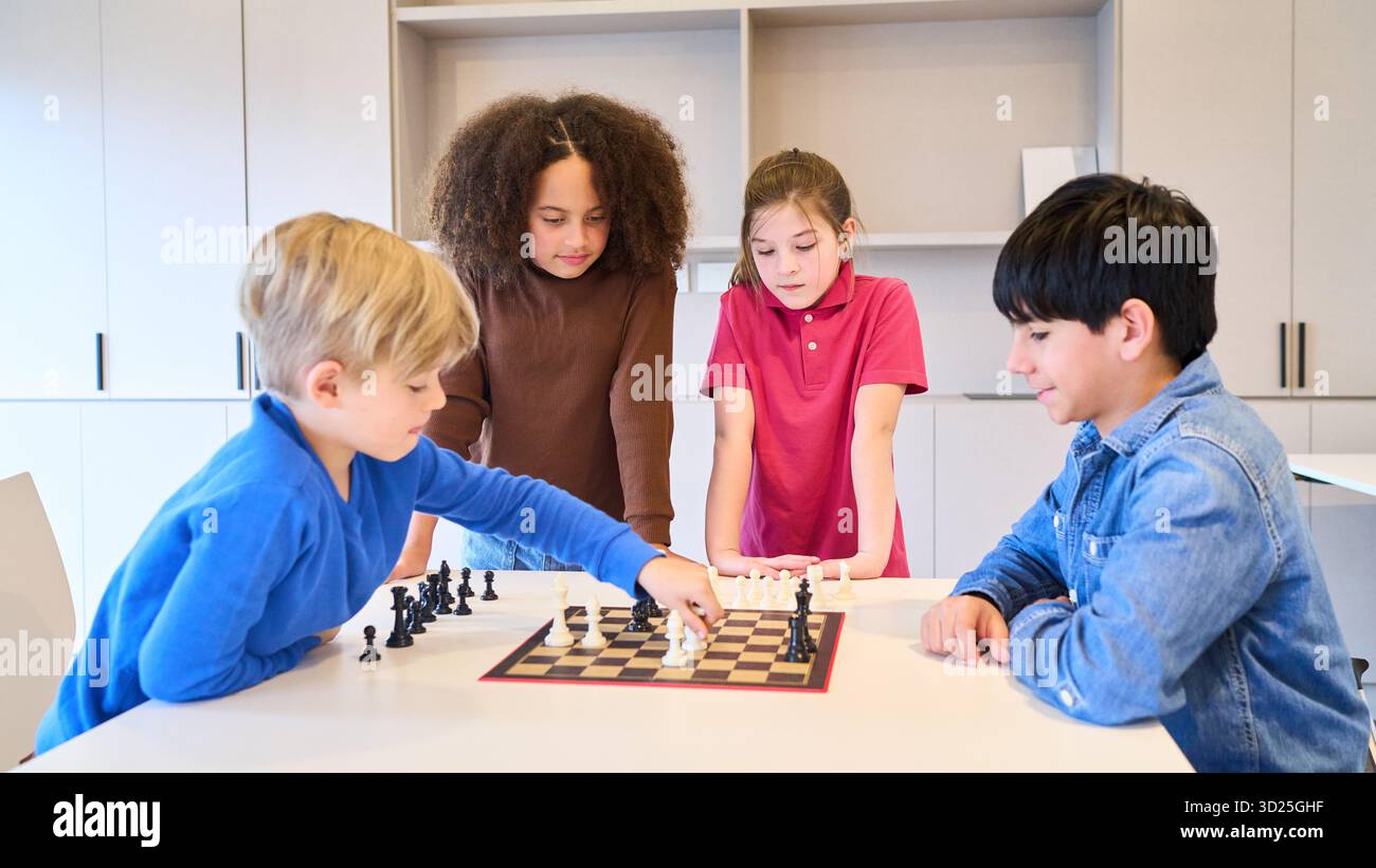 Un gruppo eterogeneo di bambini si riunisce intorno a una scacchiera, impegnandosi in un gioco concentrato mentre partecipi a un'attività terapeutica supervisionata presso un pediat Foto Stock