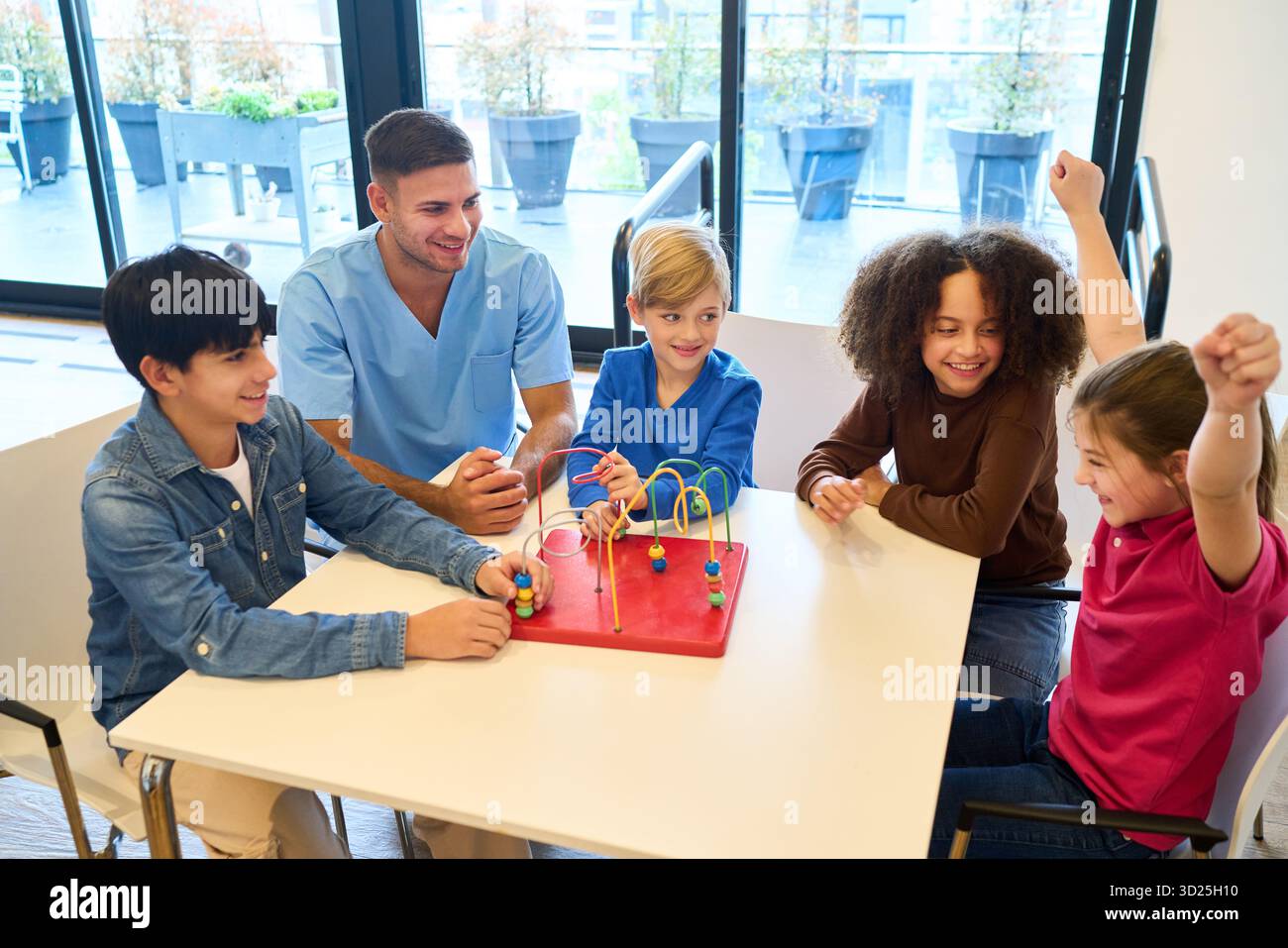 Un medico guida un gruppo di bambini in un'attività giocosa di abilità motorie in un ambiente di riabilitazione pediatrica, promuovendo l'equilibrio, la coordinazione e i cooperati Foto Stock