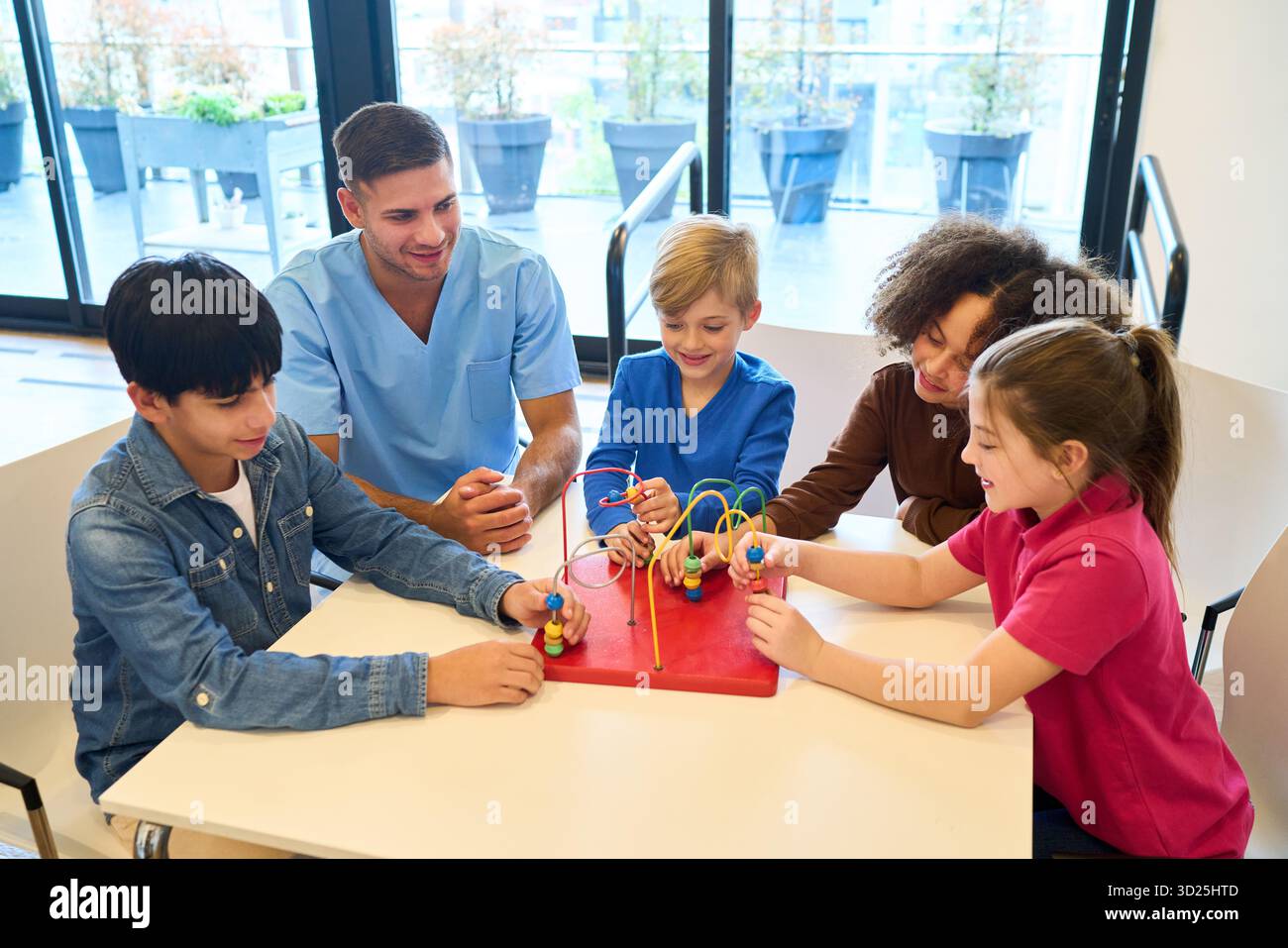 Un gruppo di bambini e un terapeuta partecipano a una sessione clinica brillante, utilizzando un labirinto di perle e attività ludiche per costruire abilità motorie, equilibrio, a. Foto Stock