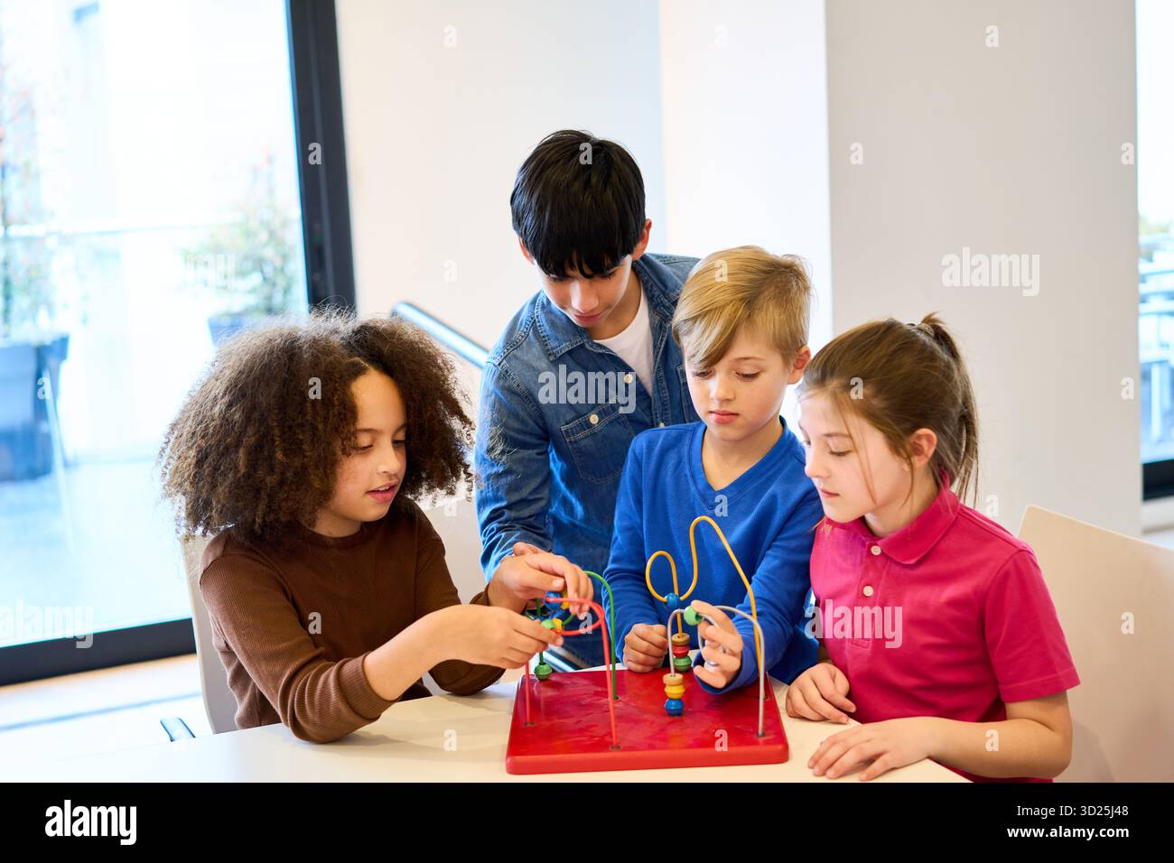 Un piccolo gruppo di bambini partecipa a un'attività di riabilitazione presso una clinica, guidata da un operatore sanitario o da un terapeuta. Usano un labirinto di perle per migliorare la co Foto Stock