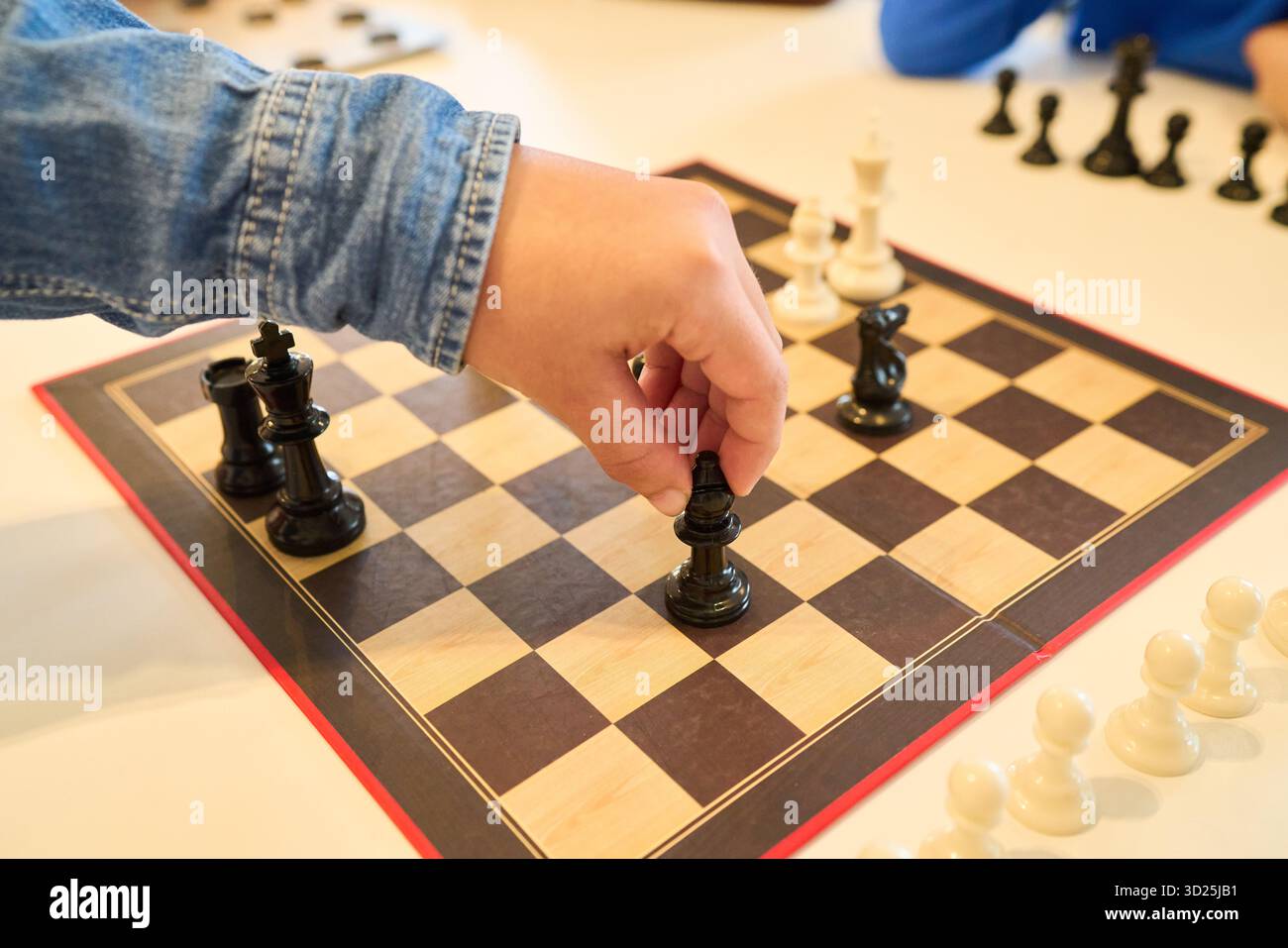 Un bambino muove una scacchiera nera su una scacchiera di legno, concentrata durante una partita in famiglia. La scena cattura concentrazione, apprendimento e delicati competi Foto Stock