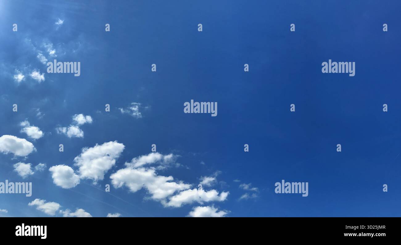 Una tranquilla vista panoramica di un cielo blu con nuvole bianche sparse, perfetta per testate o disegni di sfondo. Cattura un'atmosfera tranquilla e ariosa Foto Stock