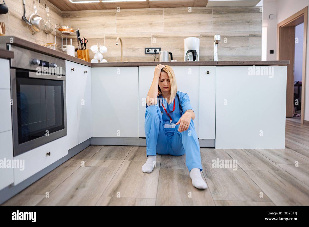 Dottore esausto seduto sul pavimento in cucina, sentendosi giù Foto Stock