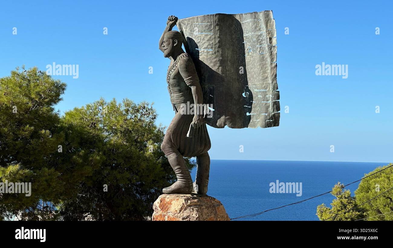 Eroica statua in bronzo di Spyros Kayales che innalza la bandiera greca al parco Venizelos Graves di Akrotiri, Chania, Creta, Grecia, con sfondo marino. Foto Stock