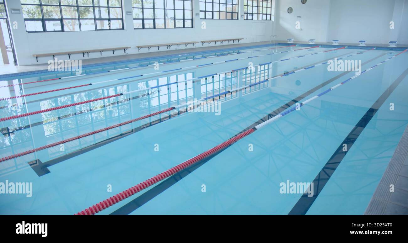 Piscina vuota che occupa la sala della piscina centrale, con divisori di corsia rossi e blu e panca in legno Foto Stock