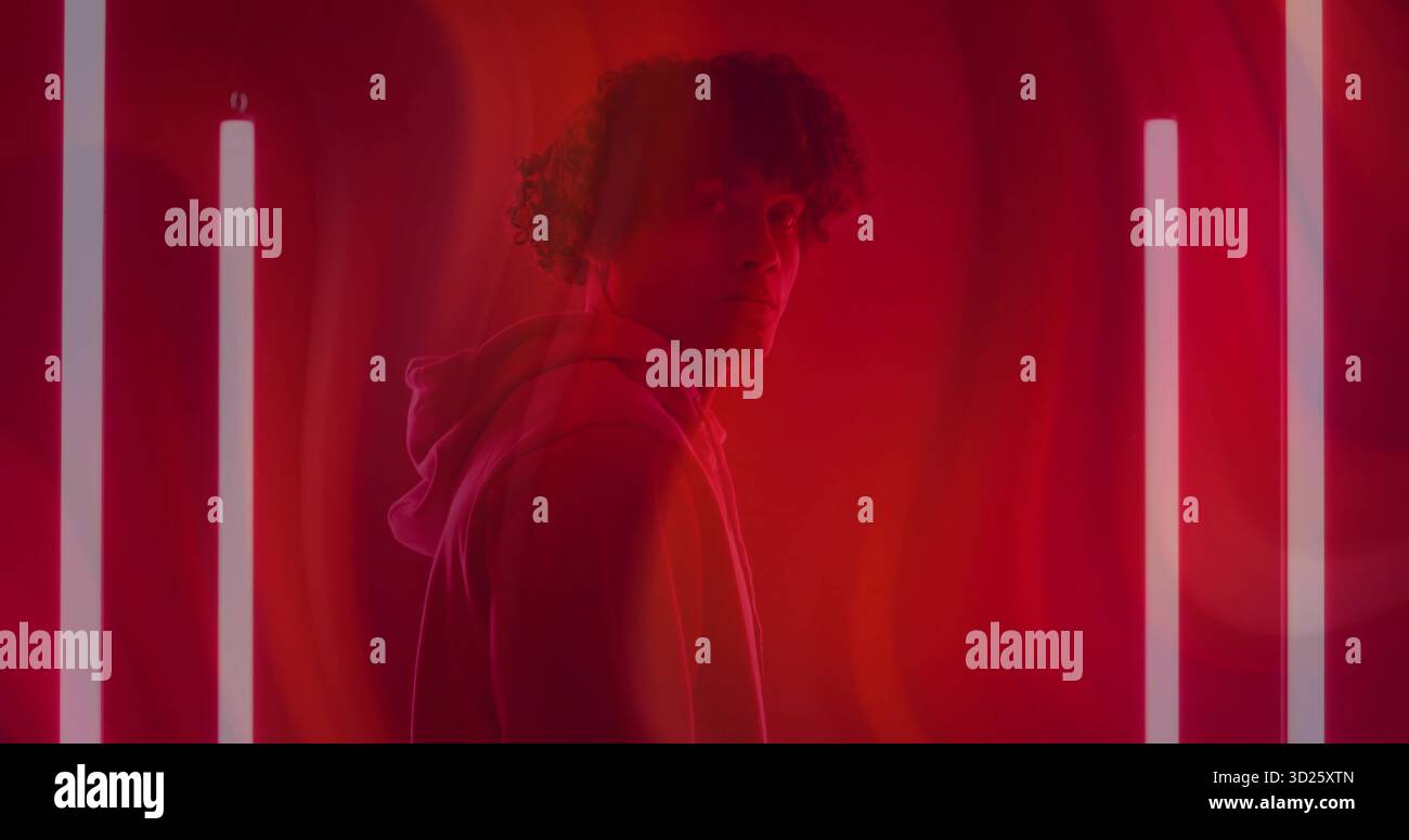 Modello maschile in piedi che indossa una felpa con cappuccio in studio immersa nella luce rossa, con tubi al neon bianchi Foto Stock