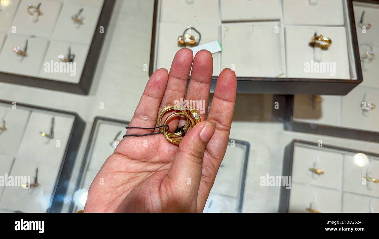 mani dei consumatori che esaminano diversi stili di fasce in oro giallo Foto Stock