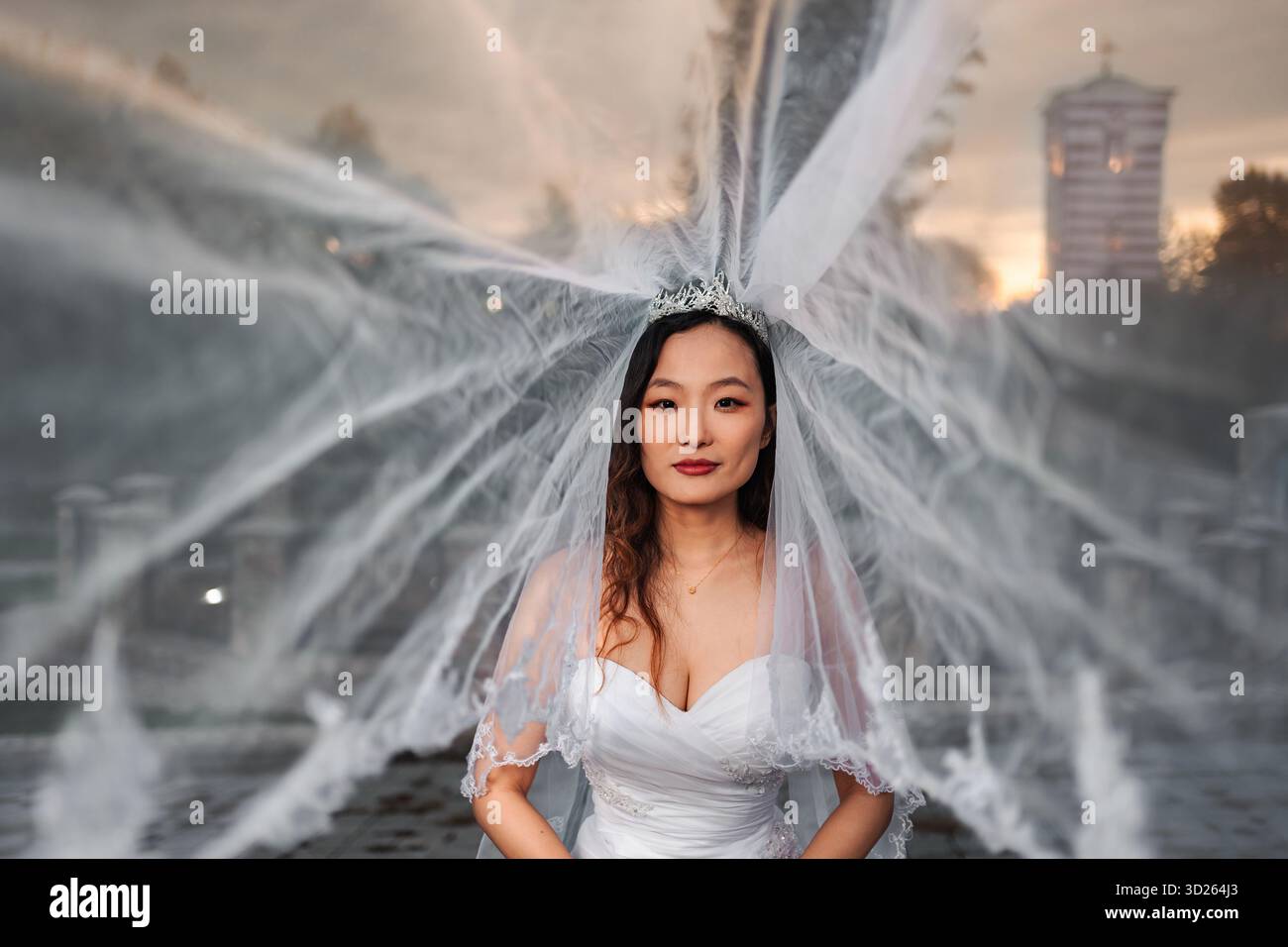 Sposa cinese con abito da sposa e velo accanto alla fontana Foto Stock