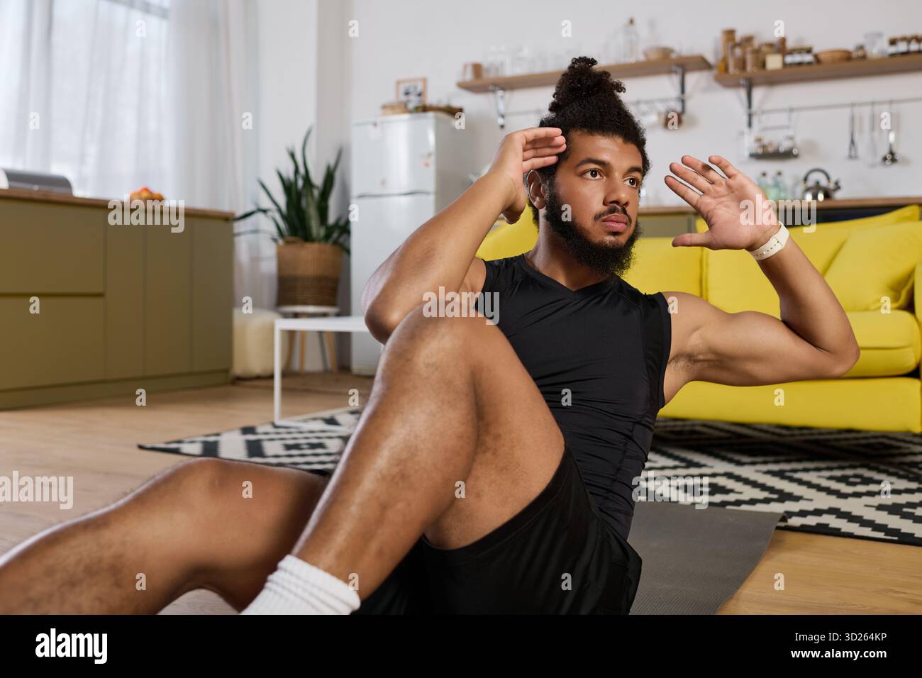 Uomo concentrato con capelli ricci e barba esegue esercizi al centro in uno spazio luminoso. Foto Stock