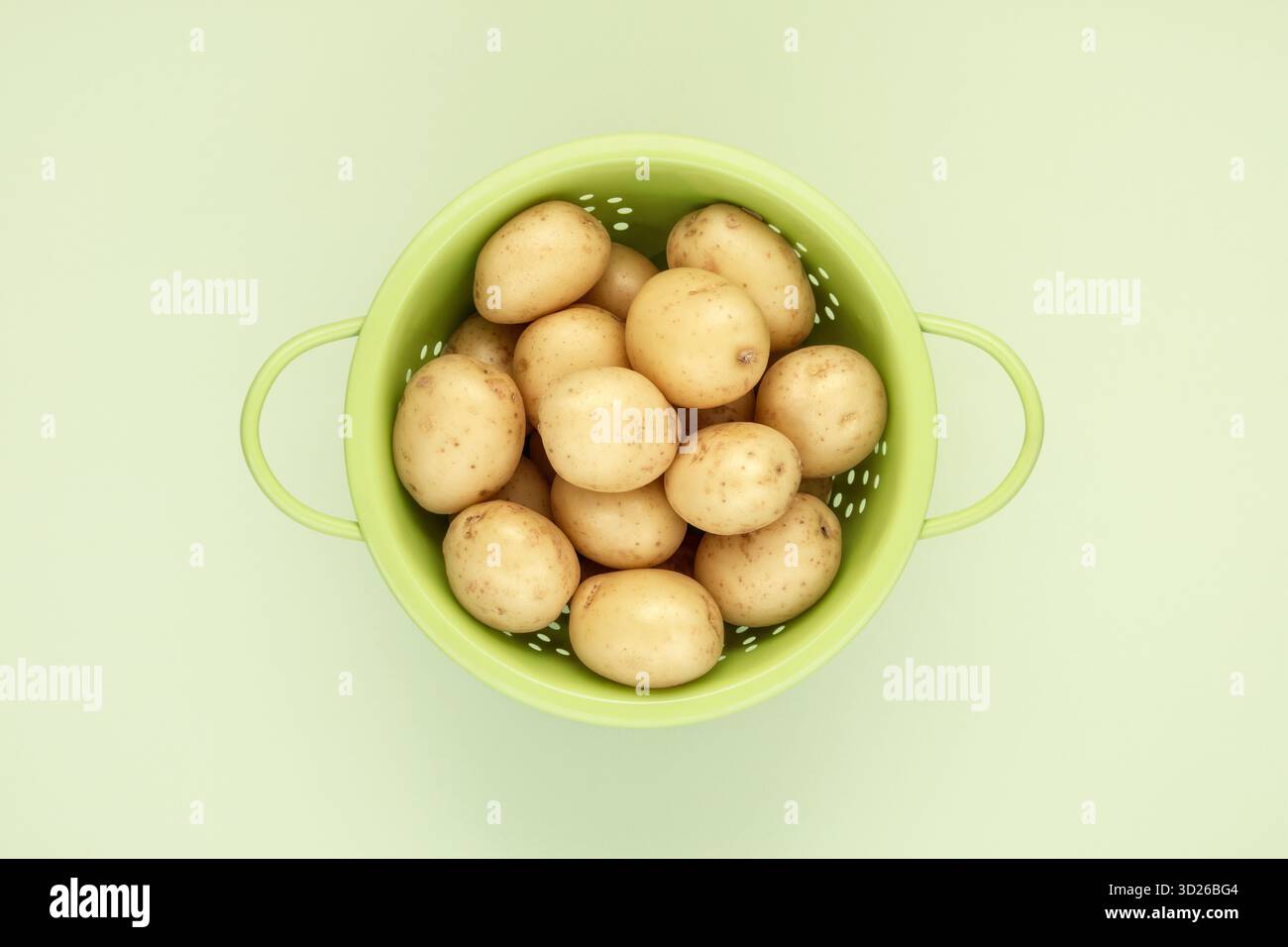 Patate crude fresche in colino verde su sfondo verde liscio Foto Stock
