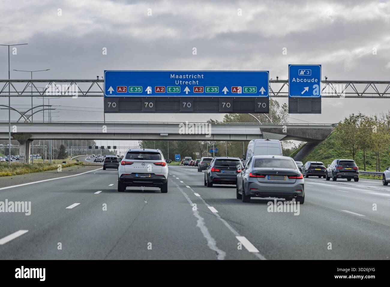 Un'autostrada A2 olandese affollata che mostra un cartello sospeso che dirige il traffico verso Maastricht e Utrecht, con tutte le corsie principali attualmente limitate a 70 km/h sp Foto Stock