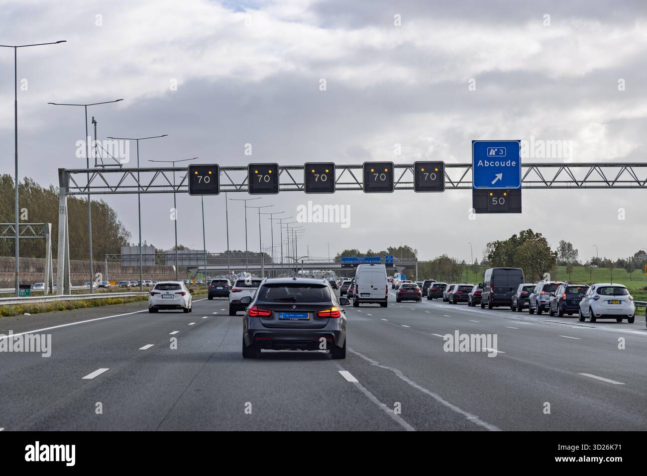 Vista di un'autostrada olandese a più corsie con segnali a messaggio variabile in testa che mostrano un limite di velocità di 70 km/h a causa delle condizioni del traffico. Foto Stock