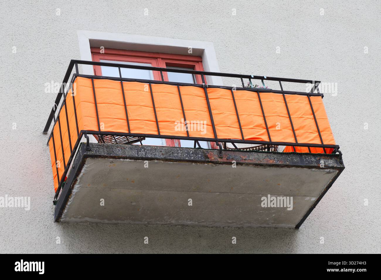 Vista ad angolo basso di un balcone vintage con tessuto arancione montato su una ringhiera di ferro nera. Foto Stock