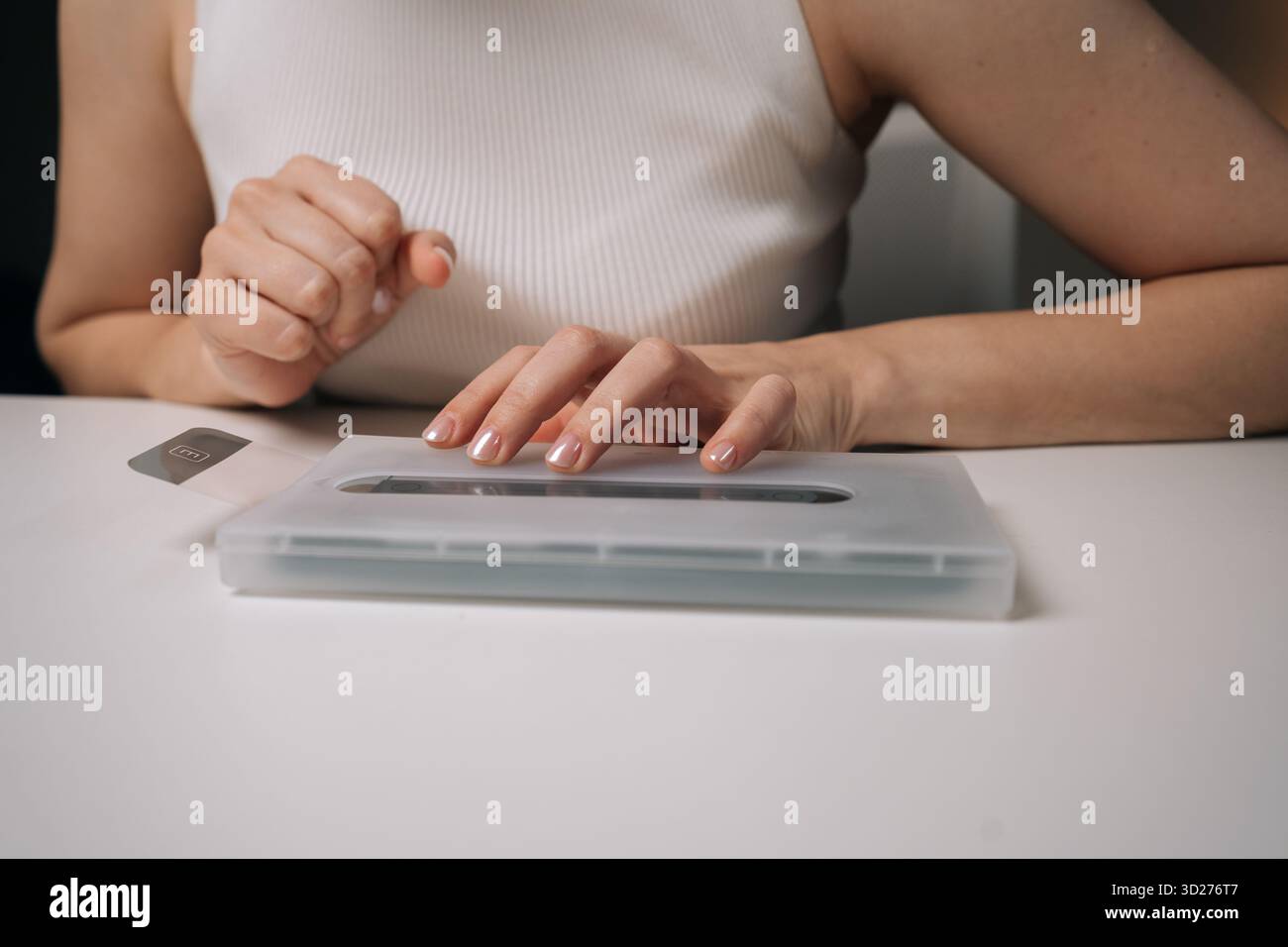 Tecnico femminile che utilizza una macchina specializzata per applicare con precisione la pellicola protettiva in vetro sullo schermo dello smartphone, garantendo la massima copertura e protezione Foto Stock