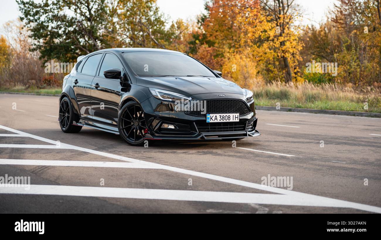 Black ford Focus su una strada nella foresta autunnale. Vista frontale di tre quarti della berlina compatta e sportiva sulla strada rurale al tramonto. Foto Stock