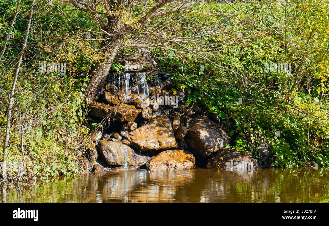 Una piccola cascata è circondata da rocce e alberi. L'acqua è marrone e anche le rocce sono marroni. La scena è tranquilla e serena Foto Stock