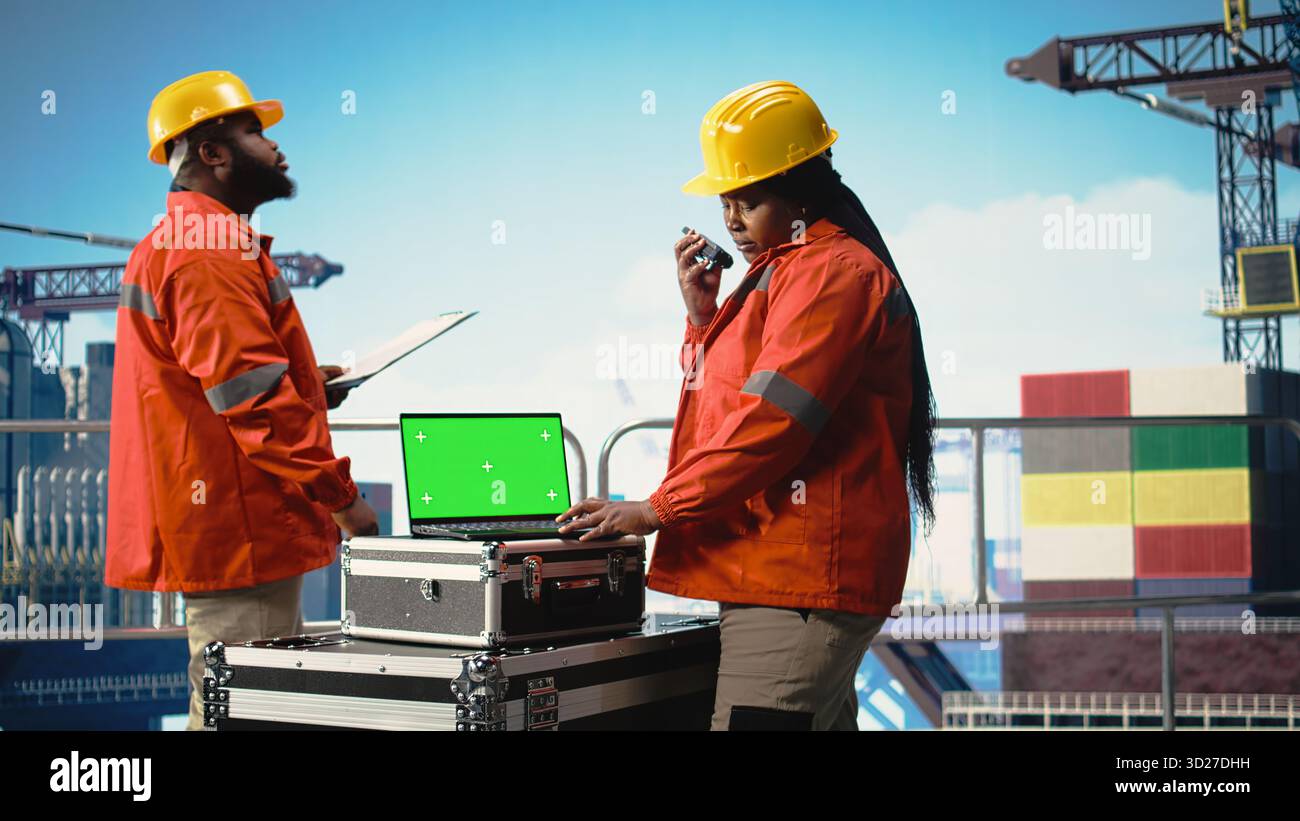 Computer portatile con schermo verde utilizzato dal lavoratore della macchina perforatrice che tiene in mano un dispositivo radio portatile per monitorare il funzionamento. Donna sul ponte piattaforma offshore che utilizza walkie talkie e notebook mockup, attrezzatura di taratura, Foto Stock