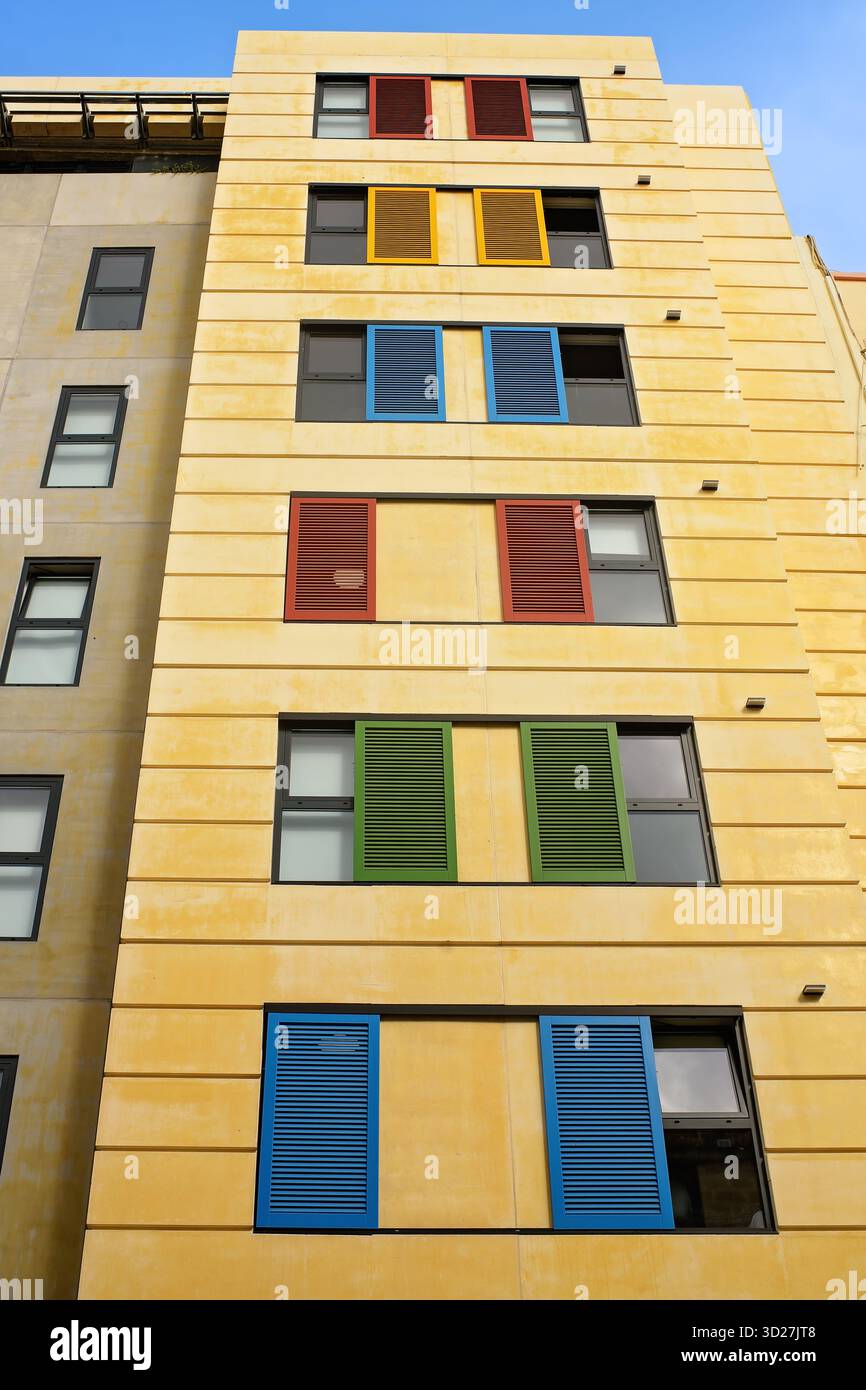 Persiane colorate in legno su strette finestre di un edificio residenziale giallo a più piani contro un cielo blu. Foto Stock
