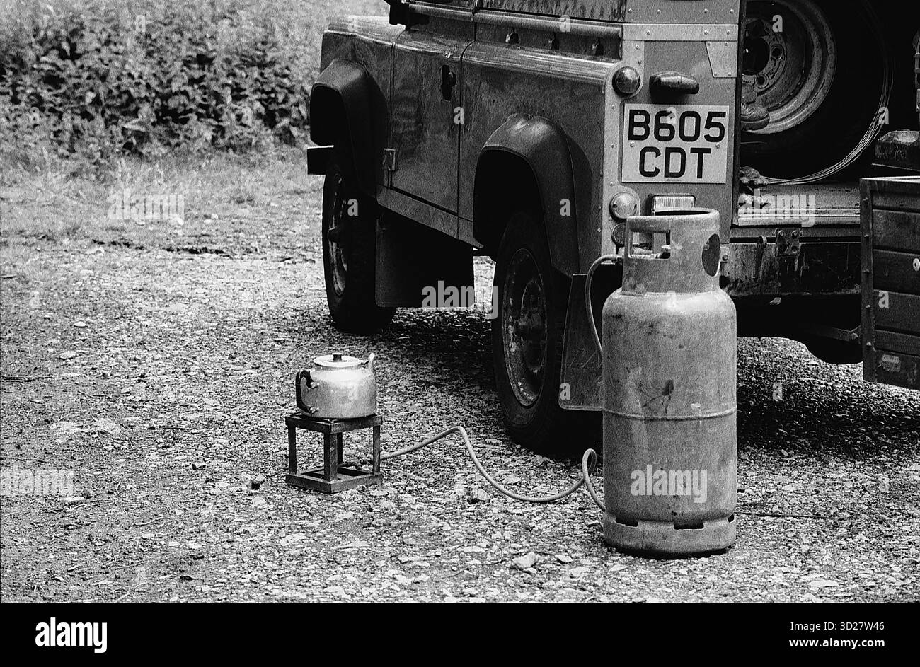 L'immagine raffigura una stufa a propano con un bollitore posizionato su un piccolo supporto in metallo. Un serbatoio di propano è posizionato accanto alla stufa, collegato da un tubo flessibile. La scena sembra essere all'aperto, con un veicolo parzialmente visibile sullo sfondo, Inghilterra, Regno Unito Foto Stock