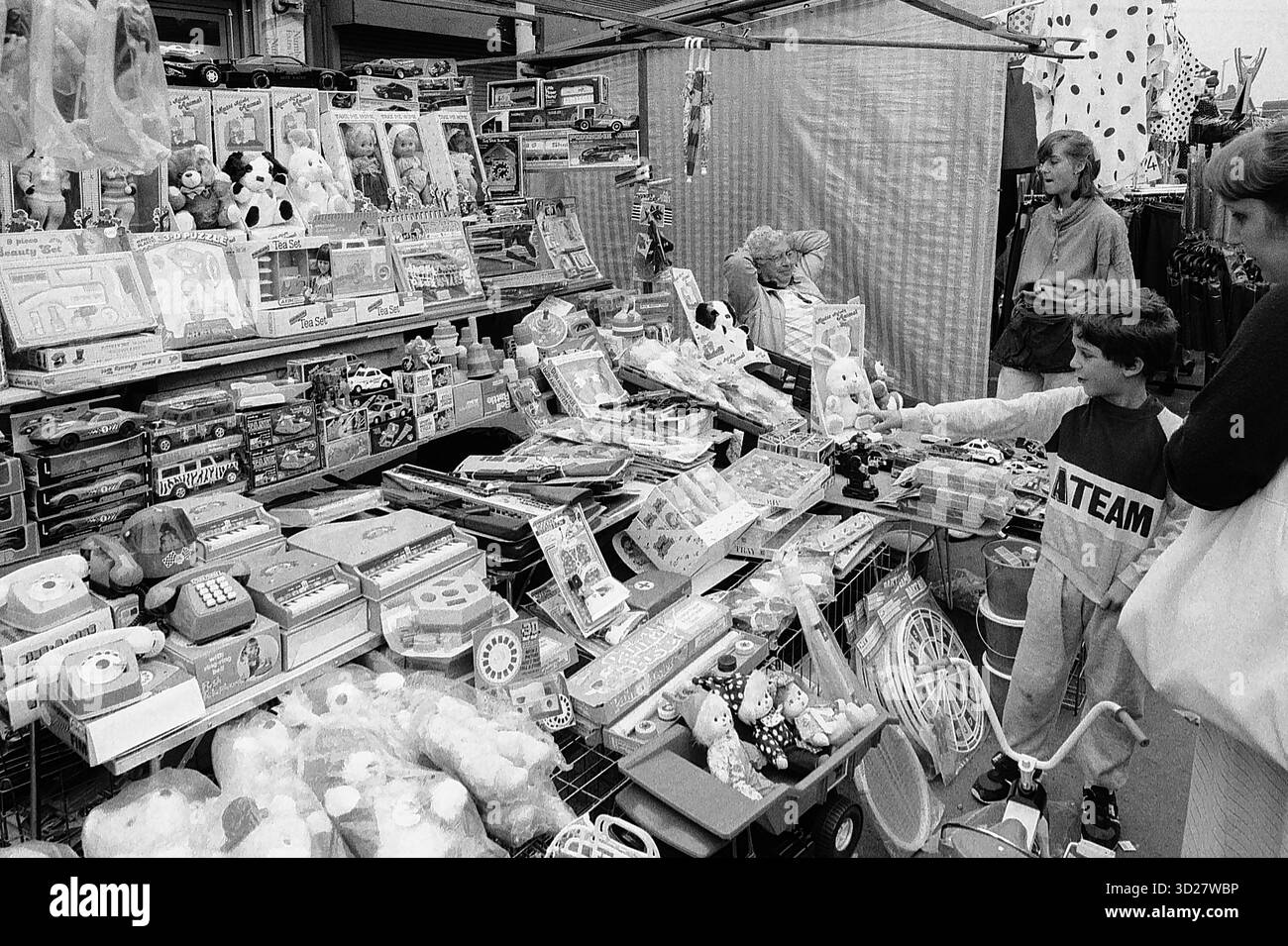 Una scena movimentata al Camden Lock Market, Londra. Gli amanti dello shopping curiosano in una collezione diversificata di giocattoli e cimeli vintage, creando una vibrante istantanea di questa iconica destinazione londinese. L'eclettico mix di merci e l'atmosfera vivace del mercato sono una caratteristica distintiva del carattere unico di Camden. Foto Stock