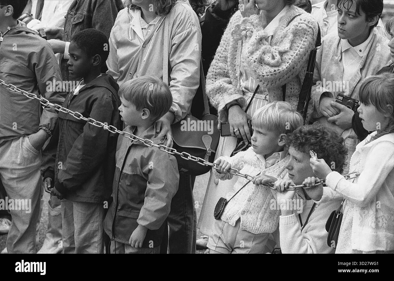 Un momento spontaneo di fidanzamento giovanile si svolge alla Horse Guards Parade di Londra. I bambini interagiscono giocosamente con una catena cerimoniale, catturando un'autentica espressione di partecipazione pubblica durante un evento storico. La location iconica, immersa nella tradizione e nella storia militare, offre uno sfondo unico a questa scena candida. Foto Stock