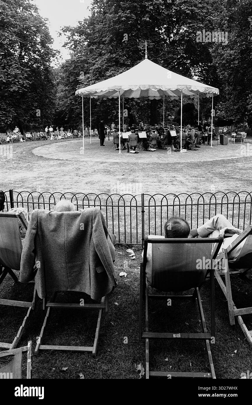 Hyde Park, Londra, 1986. Una scena tranquilla si svolge sotto l'iconica tribuna, un punto focale di questo storico spazio verde. I musicisti si esibiscono per un pubblico godendosi un pomeriggio estivo in uno dei parchi più amati di Londra. Foto Stock