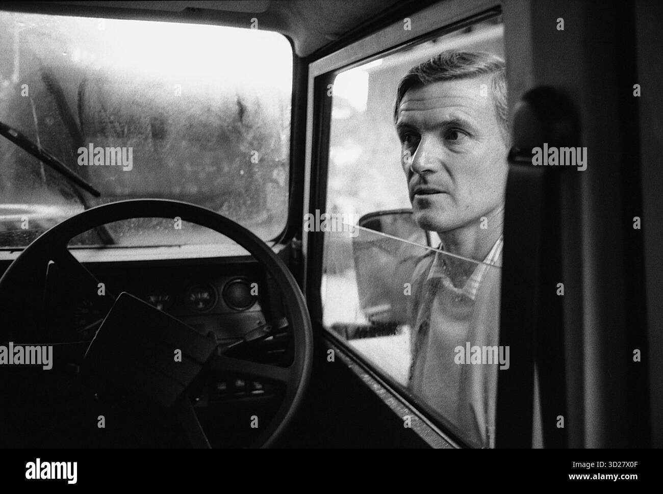Guida maschile che guarda in vetrina di una Land Rover, Tanzania. Il parabrezza dalle striature di pioggia offre un riflesso distorto del paesaggio circostante, sottolineando l'isolamento e l'immensità della natura selvaggia africana. L'immagine evoca un senso di contemplazione tranquilla, invitando lo spettatore a considerare l'esperienza dell'esplorazione e la profonda connessione tra uomo e natura. Foto Stock