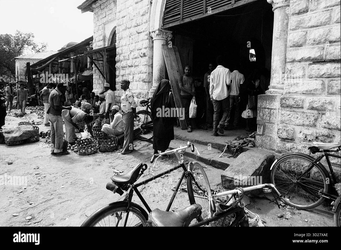 La vivace scena del mercato di Zanzibar è stata catturata in bianco e nero. Gli acquirenti e i venditori si riuniscono intorno alle bancarelle, creando una vibrante istantanea del commercio quotidiano nella storica Stone Town. Foto Stock