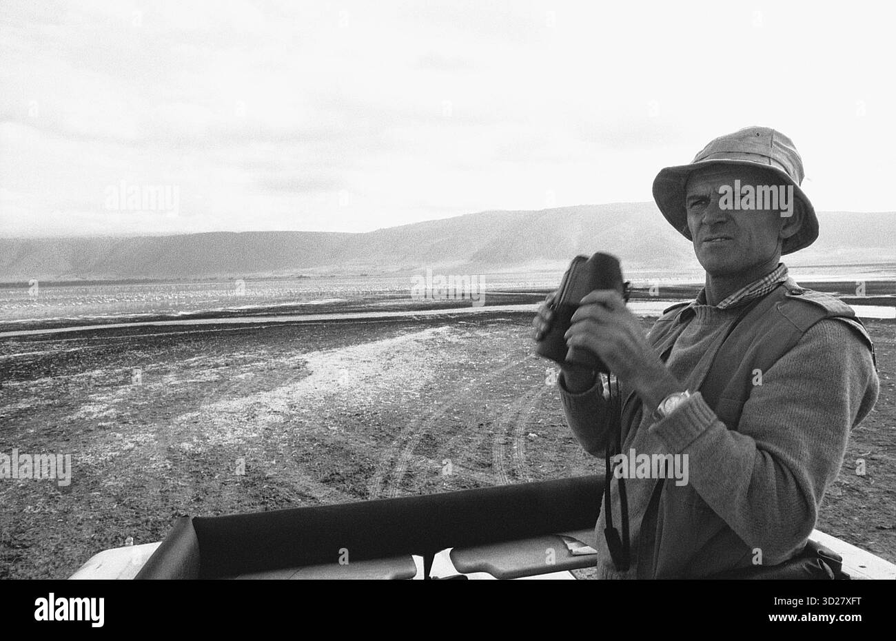 Safari Guide osserva il paesaggio del cratere. Una guida esperta di safari esplora l'ampio terreno del Parco Nazionale del cratere di Ngorongoro in Tanzania, utilizzando un binocolo per scansionare il lontano paesaggio vulcanico. Il parco, patrimonio dell'umanità dell'UNESCO, è rinomato per la sua variegata fauna selvatica e le formazioni geologiche uniche. Foto Stock
