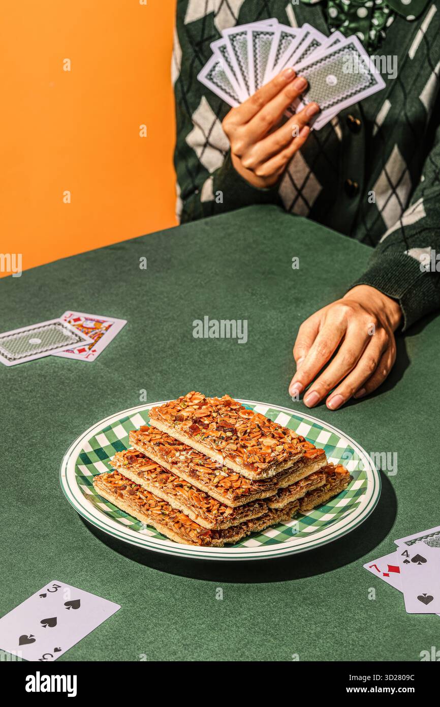 : Gioco di poker a tema Nut fragile Pila su piatto a scacchi con carte da gioco e mano su tavolo verde Foto Stock