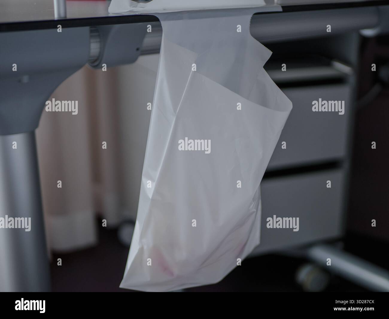 Fotografia ravvicinata di un sacchetto di plastica bianco appeso a un supporto per apparecchiature ospedaliere all'interno di una stanza del paziente. L'ambiente medico suggerisce l'igiene Foto Stock