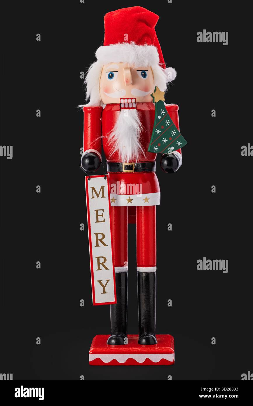 Festive Red Schiaccianoci di Babbo Natale che tiene in mano la targhetta regalo e l'ornamento dell'albero di Natale isolato sul nero Foto Stock