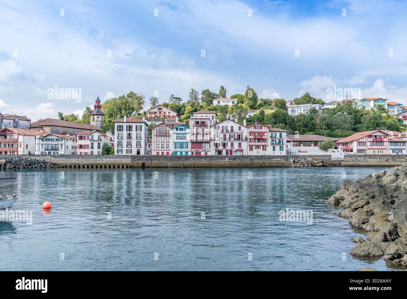 Case basche tradizionali colorate, porto di Saint-Jean-de-Luz, Paesi baschi francesi, torre della chiesa, architettura sul lungomare, calme acque della baia Foto Stock
