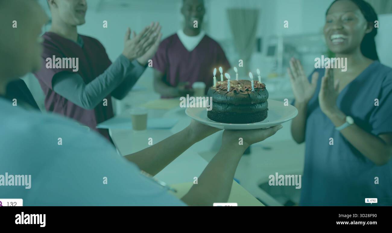 L'infermiera che tiene in mano una torta al cioccolato a due livelli con candele accese nella sala con il applauso del team Foto Stock