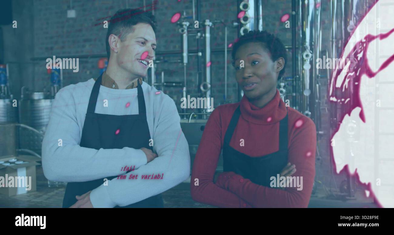 Chiacchierando con il personale del birrificio indossando grembiuli neri che incrociano le braccia nell'area del birrificio, con vasche di fermentazione Foto Stock