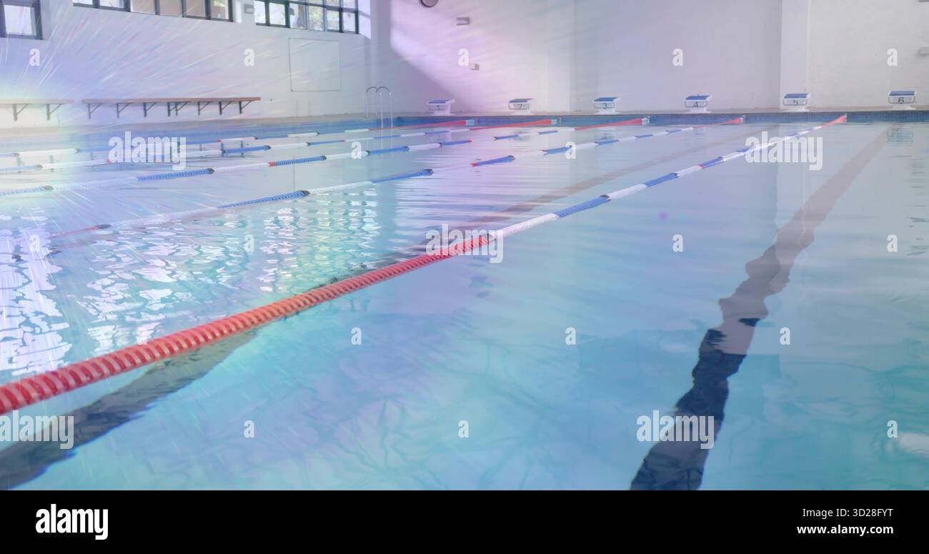 Mostra una piscina vuota che riflette il sole, fiancheggiata da corde e scale nel centro acquatico Foto Stock