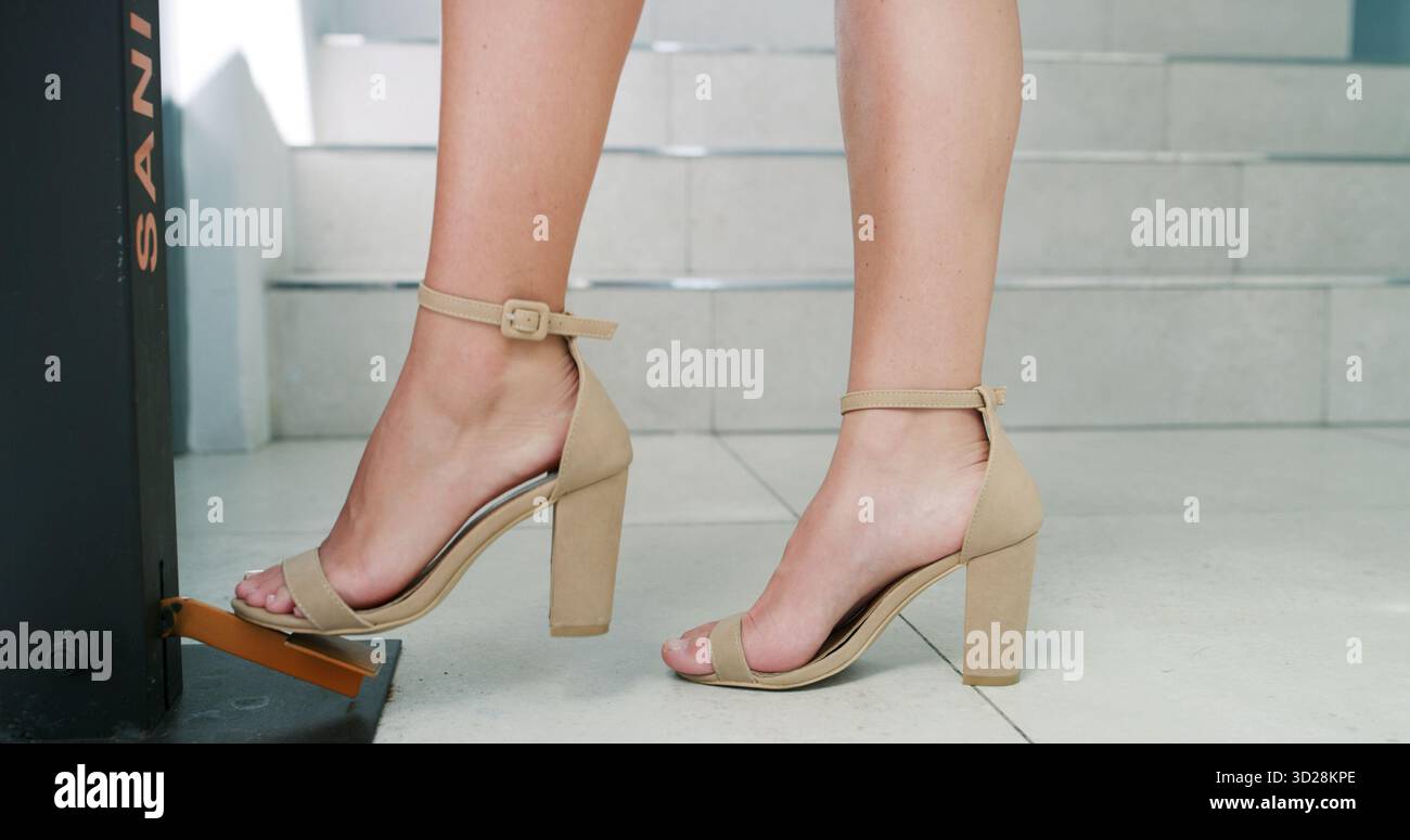 Donna, piede e igienizzatore dispenser per la salute, il benessere o la prevenzione dei virus con i tacchi. Piedi, sanitari o persone con igiene in ufficio, batteri Foto Stock