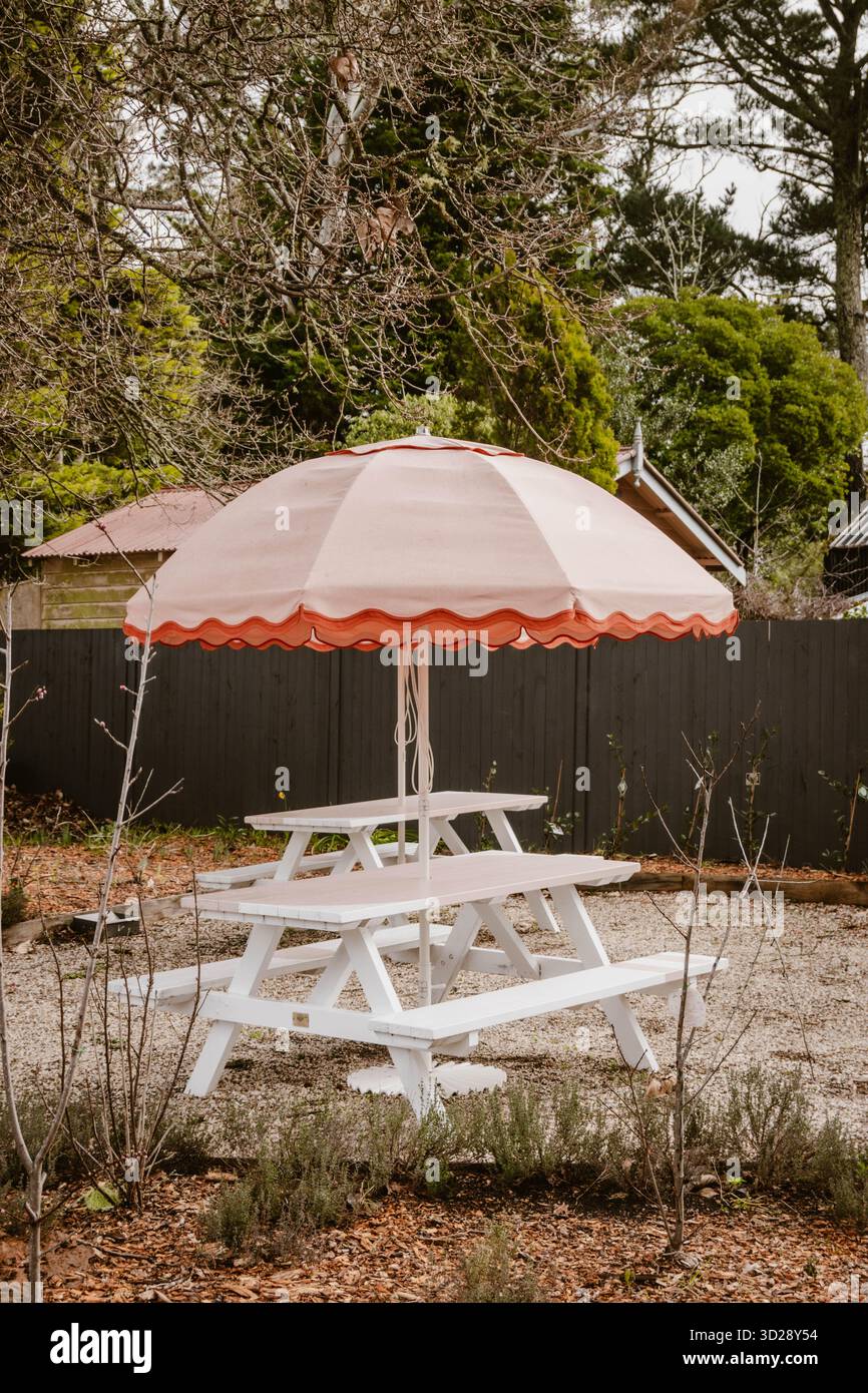 Tavoli da picnic bianchi con ombrellone rosa vintage in giardino Foto Stock
