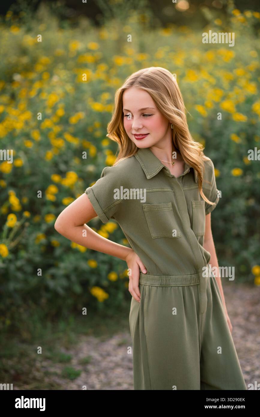 Ragazza in tuta verde posa nel campo di fiori selvatici gialli Foto Stock