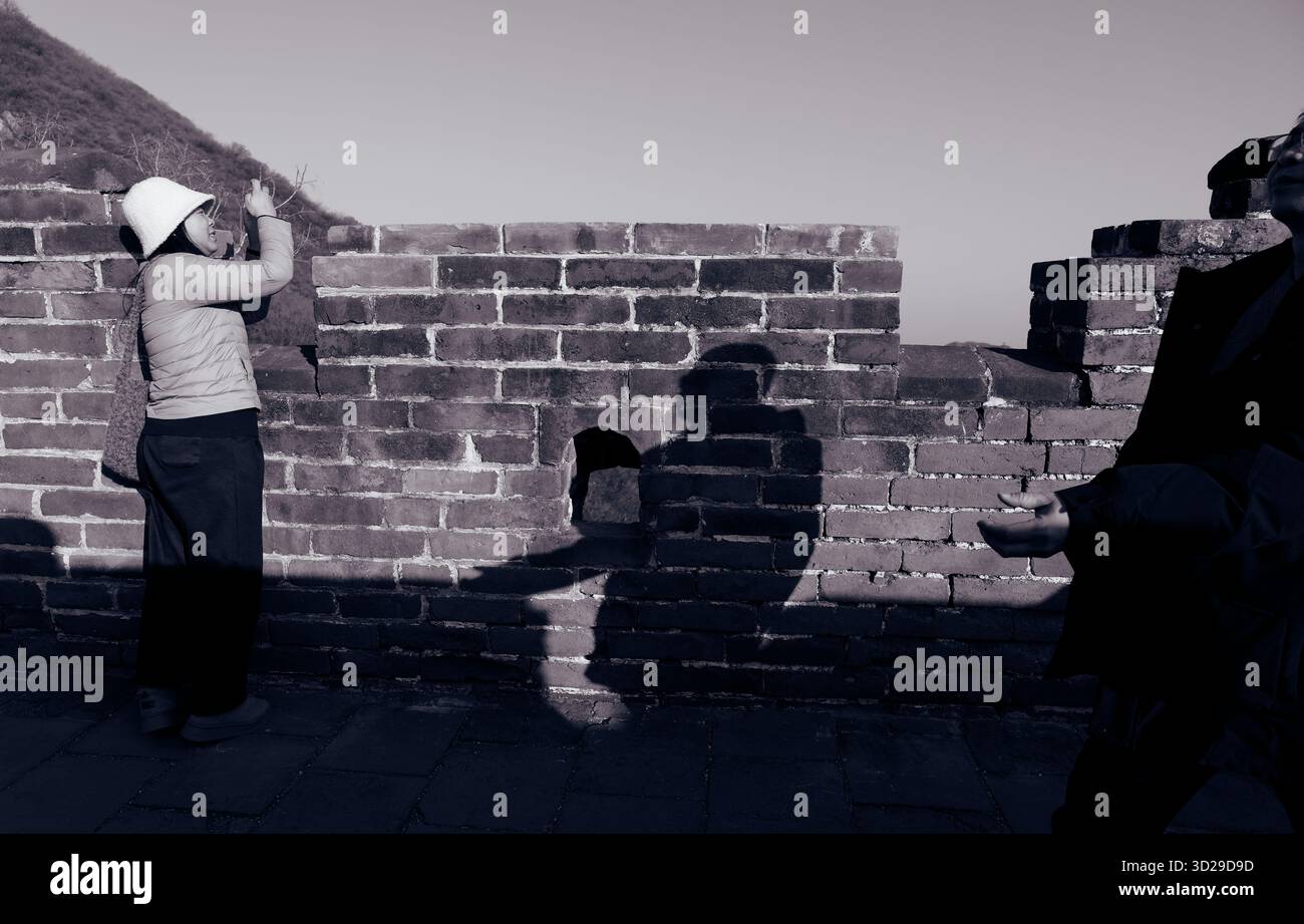 Una donna con un cappello bianco cattura una foto dalla grande Muraglia, mentre la luce del pomeriggio proietta silhouette sorprendenti Foto Stock
