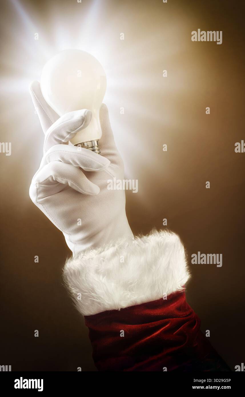 Concetto di immaginazione e buone idee a Natale con la mano di Babbo Natale che tiene una lampadina e scintilla su uno sfondo marrone isolato. Foto Stock