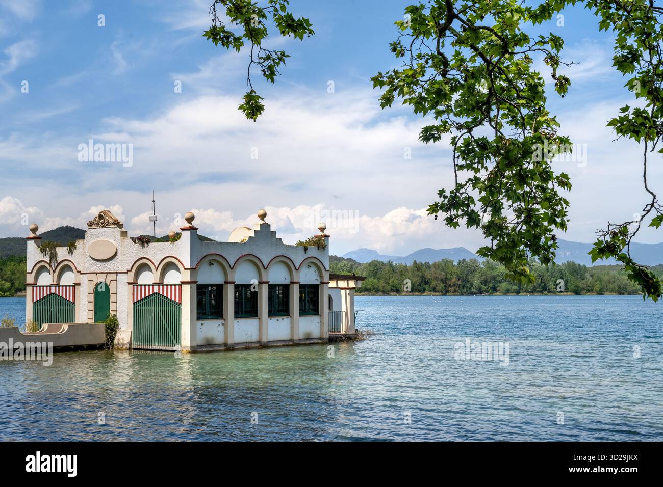 Storica pensione bianca sulle rive del lago Banyoles, Catalogna, Spagna, con acque calme e montagne sullo sfondo Foto Stock