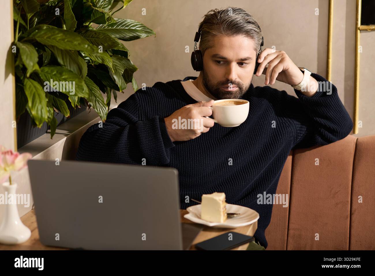 Un bell'uomo si rilassa con una tazza di caffè, concentrandosi sul suo portatile in un elegante caffè. Foto Stock